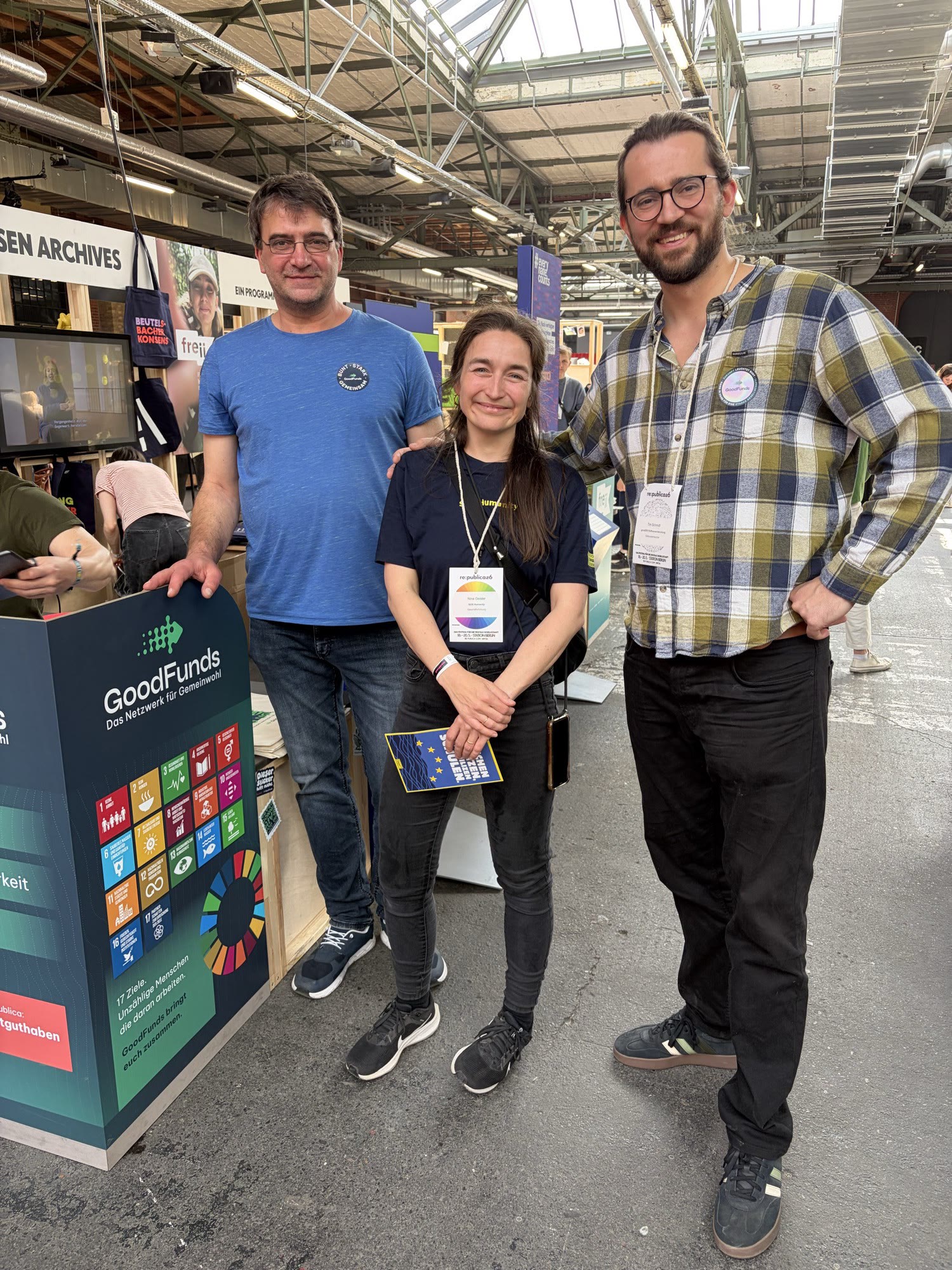 Drei Personen von SOS Humanity und GoodFunds stehen am gemeinsamen Messestand mit GoodFunds-Roll-up auf der re:publica 2026